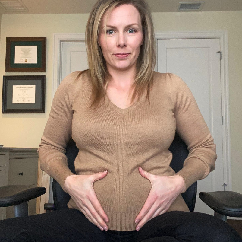 A pregnant woman who is sitting down and holding their round belly.